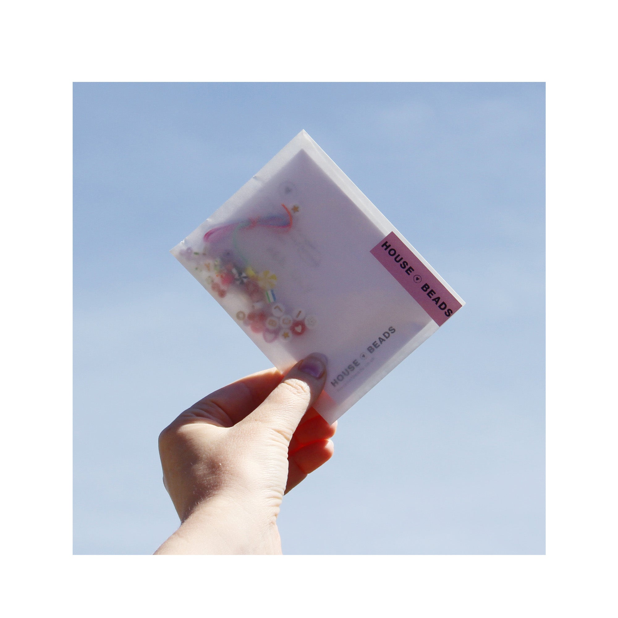 Hand holding a friendship bracelet kit against a blue sky
