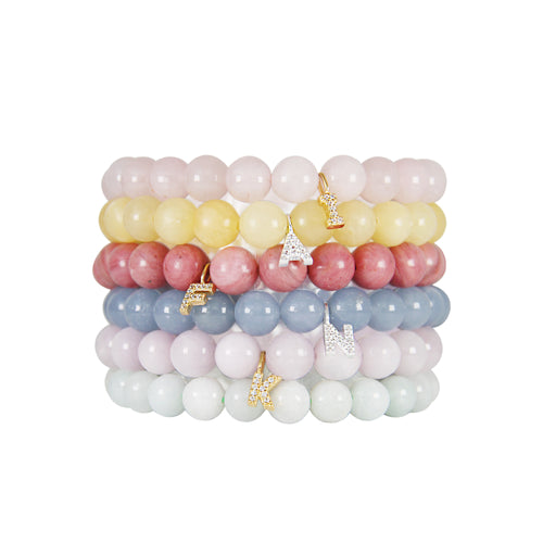 Stack of colourful semi precious beaded bracelets with silver and gold initial charms, photographed on a white background